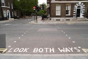 A street in London with the phrase LOOK BOTH WAYS painted on the road, indicating the pedestrian crossing. Traffic lights are visible, showing a red signal, and classic London style buildings d photo