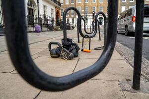 A kettlebell is secured to a bike rack on a quiet city sidewalk, drawing attention in the everyday urban scene. g photo
