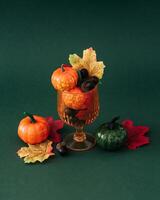 Autumn scene of cocktail glass full of colorful autumn leaves, pumpkins and nuts on green background. Minimal creative Fall party concept. Festive holiday layout. photo