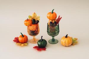 Autumn scene of two cocktail glasses full of colorful autumn leaves, pumpkins and nuts on beige background. Minimal creative Fall party concept. Festive holiday layout. photo