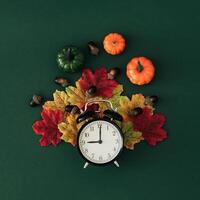 Autumn composition made with colorful autumn leaves, pumpkins, nuts and retro alarm clock on green background. Creative autumn time concept. Fall aesthetic. Flat lay style. Top view. photo