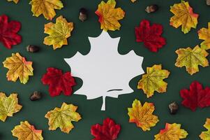 Trendy autumn pattern made of colorful autumn leaves and nuts on green background with leaf shape paper card note. Seasonal concept. Creative copy space. Nature flat lay. Top view banner. photo