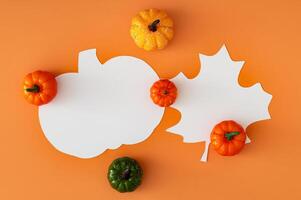 Creative autumn layout made with colorful pumpkins and leaf and pumpkin shape paper card note copy space on orange background. Minimal season concept. Fall aesthetic. Flat lay style. Top view banner. photo