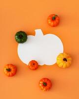 Creative autumn layout made with colorful pumpkins and pumpkin shape paper card note copy space on orange background. Minimal season concept. Fall aesthetic. Flat lay style. Top view banner. photo
