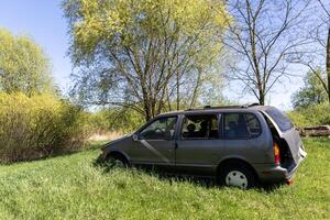 Abandoned passenger car with flat tires and broken windows on green grass. Poland photo