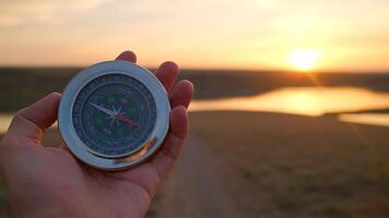 Hand holding compass during sunset over river landscape representing navigation and exploration concepts photo
