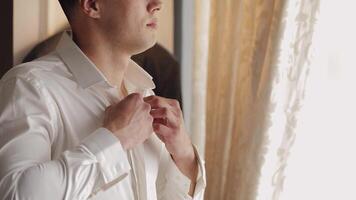 Stylish man in jacket fastens buttons, buttoning white shirt preparing to go out near window video