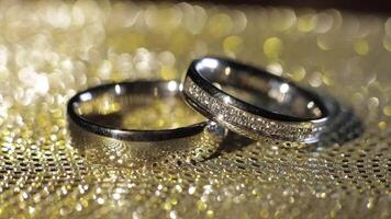 Wedding rings lying, rotate, spinning on shiny golden shining surface with light, close-up macro video