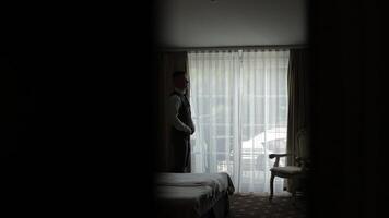 Man in jacket fastens buttons, buttoning white shirt preparing to go out, walking near window video