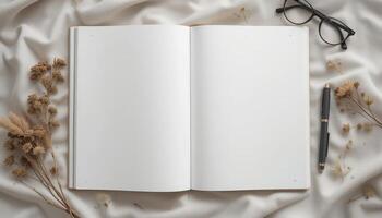 Blank Notebook Surrounded by Dried Flowers and Glasses on a Soft Fabric Background photo