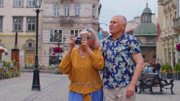 Senior old stylish tourists man woman walking, taking photos on old camera at summer city center video