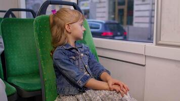 Portrait of child girl passenger riding at public modern bus or tram transport, looking out window video