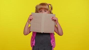 Smiling schoolgirl hiding behind a book laugh fooling around making playful silly facial expressions video