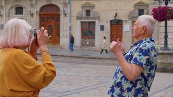 Elderly tourist grandfather taking photo pictures of grandmother on retro camera in old summer town video