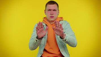 Student man in denim jacket closing eyes showing stop gesture, confused shy scared to watch video