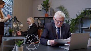 Senior elderly business company manager sitting at office reading candidate resume, job interview video
