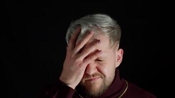 Disappointed man doing face palm gesture on black background. Stressed guy covering face with hand video
