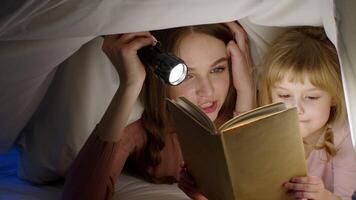 Young mother reading goodnight story fairytale to child daughter under duvet blanket in night room video