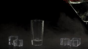 Barman hand pours vodka, tequila or sake from bottle into glass on black background with ice cubes video