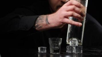 Bartender man pouring up frozen vodka, sake from bottle into shot glass with ice cubes and drinking video