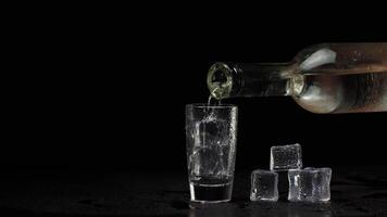 Barmann Gießen oben Schuss von Wodka mit Eis Würfel von Flasche in Schuss Glas auf schwarz Hintergrund video