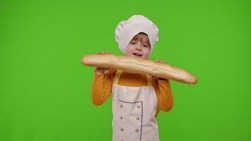 Child girl dressed in apron like chef cook baker breaking and eating fresh baguette on chroma key video