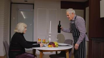 Senior retired couple having fun drinking wine and eating meal during romantic supper in kitchen video