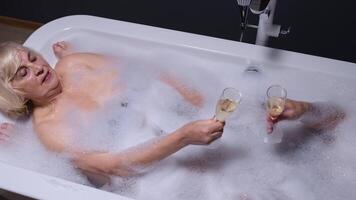 Senior couple grandfather and grandmother is taking foamy bath drinking champagne in luxury bathroom video