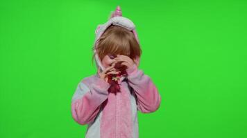 Little blonde child girl smiling, puts on sunglasses in unicorn pajamas costume on chroma key video