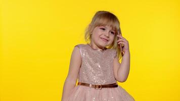 Smiling kid girl 5-6 years old using speaking talking on mobile cell phone on yellow background video