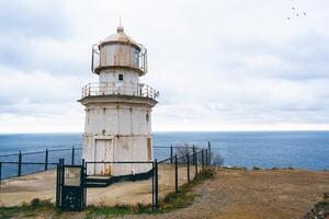 Historic lighthouse standing on a cliff overlooking the ocean under a cloudy sky photo