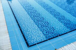 Clear blue swimming pool with tiled patterns and sunlight reflections during midday photo
