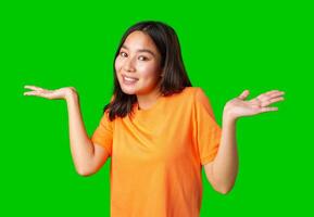 Young woman with a friendly smile gestures with hands in a bright orange shirt against a green background photo