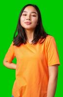 Confident young woman in orange shirt poses against bright green backdrop during studio session photo