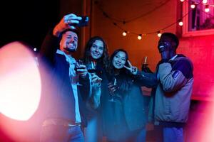 Friends enjoying a lively evening gathering with drinks and laughter under string lights in an outdoor setting photo