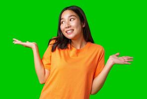Young woman in orange shirt stands with hands raised, displaying a playful expression against a green background photo