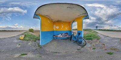 spherical seamless 360 hdri panorama inside empty concrete bus stop painted blue and yellow with tired or homeless person sleeping on bench near a bicyclein equirectangular projection, VR AR content photo