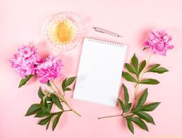 Tea, pink peonies and notebook on soft pink background. Top view, flat lay, copy space. photo