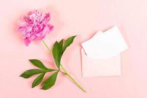Minimal flat lay with pink peony, green leaf, and open envelope on pastel background. Copy space. photo
