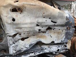 A haunting tableau of rusted, bullet-riddled civilian vehicles stacked in the photo