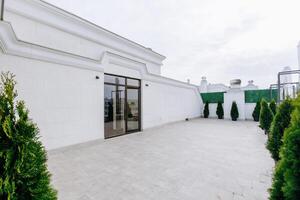 A large, elegant white building has a spacious patio and trees photo
