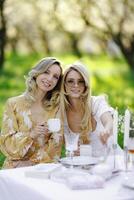 There are two women happily sitting at a table while holding cups of tea photo