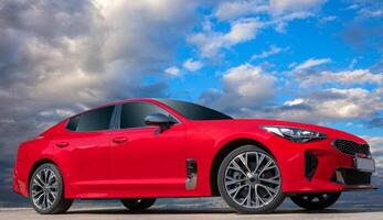 Red car on a blue sky background with white clouds. A stylish, modern, bright image of an avto mobile. photo