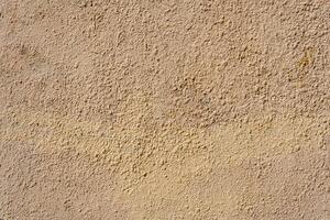 A yellow wall covered with numerous layers of plaster and paint. The layers form small irregularities and bumps. photo