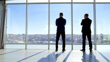 Meeting of entrepreneurs in office by the window. Rear view of two businessmen admiring the city landscape through the office window and talking about new project. video