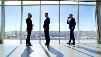 Full-length portrait of business people. Male entrepreneurs in elegant suits standing in modern office and talk about business. Profile view. Panoramic windows view on city. video