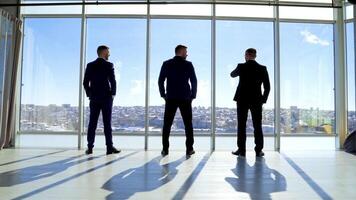 Business people in office on city landscape through window. Three men in elegant suits standing by the window and talking in sunny daytime. Back view. video