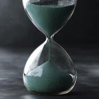 Hourglass with green sand symbolizes passage of time, evoking sense of reflection and urgency photo
