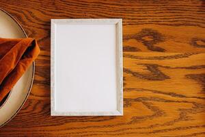 Elegant blank frame on wooden table beside a folded napkin in a minimalist setting photo