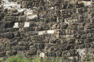 Texture of ancient stone wall covered with moss and grass in sunlight revealing history photo
